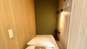 A narrow room with a bed, a wall-mounted light, and a power outlet. - Otemachi Kamon Hotel - Caters to Men - Hostel (Tokyo)