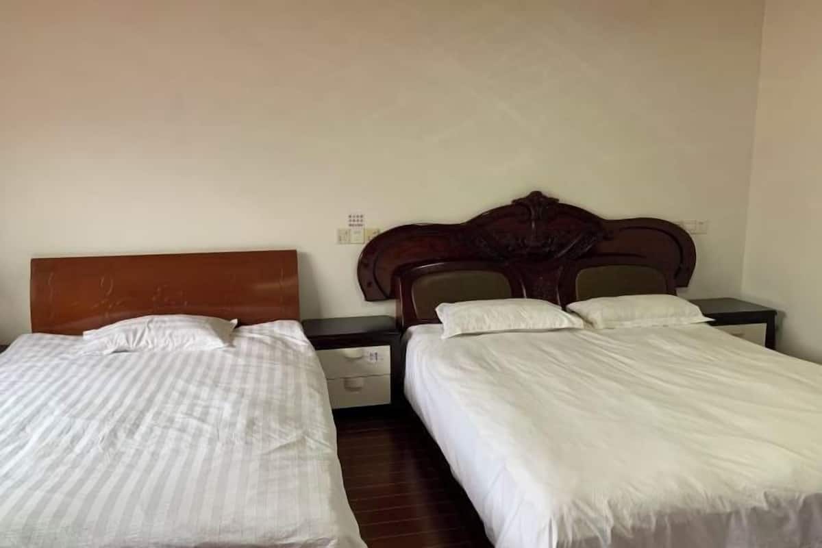 A hotel room with two single beds, wooden headboards, and a small bedside table with a lamp.
