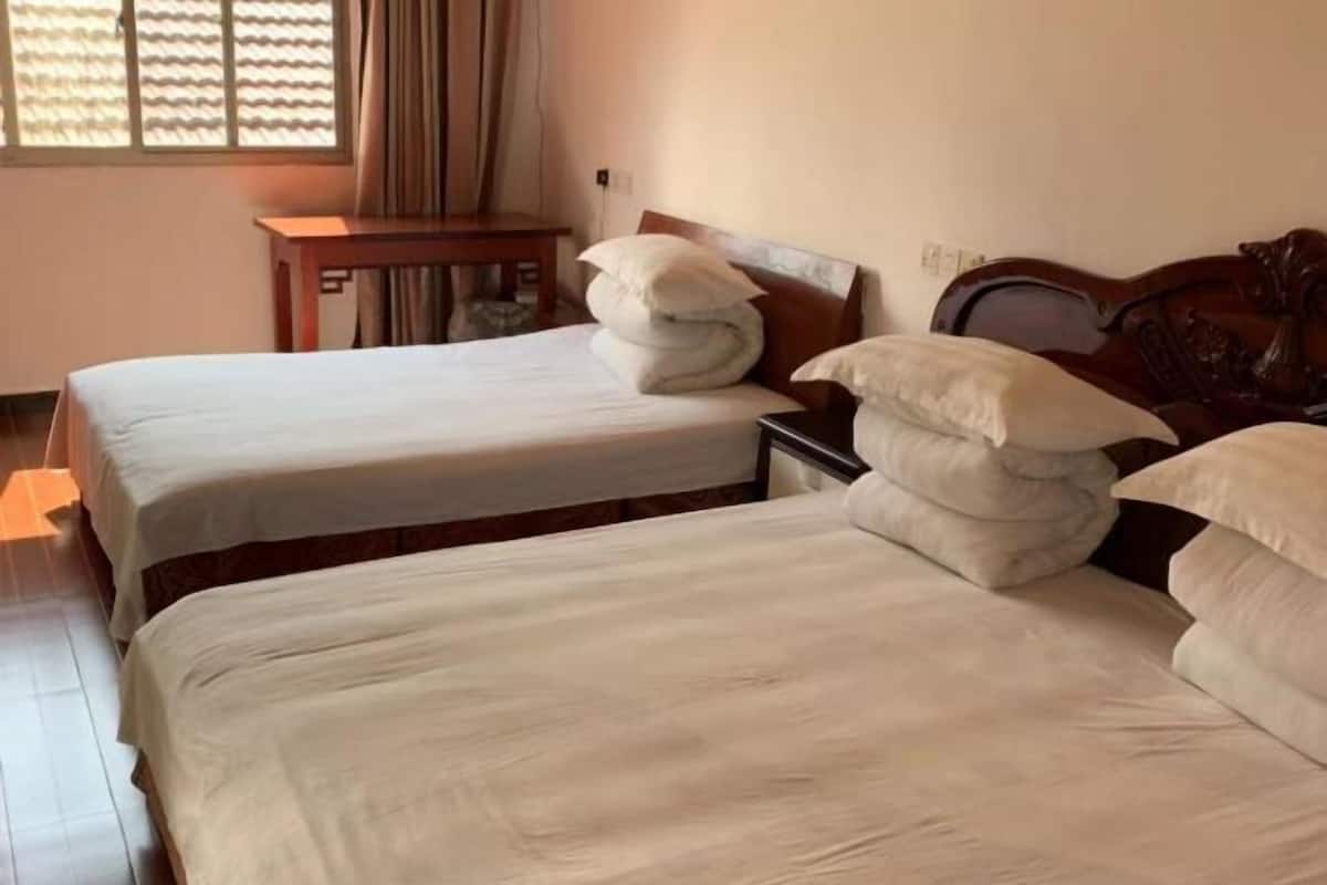 A hotel room with two beds, a small table, and a window with curtains.