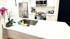 A kitchen with white cabinets, stainless steel appliances, a sink, and a bar area with stools. - Cozy Marina del Rey Stay Near the Beach (Marina del Rey)