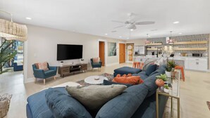 Ein modernes Wohnzimmer mit einem großen Fernseher, blauen Sofas und einem Deckenventilator.