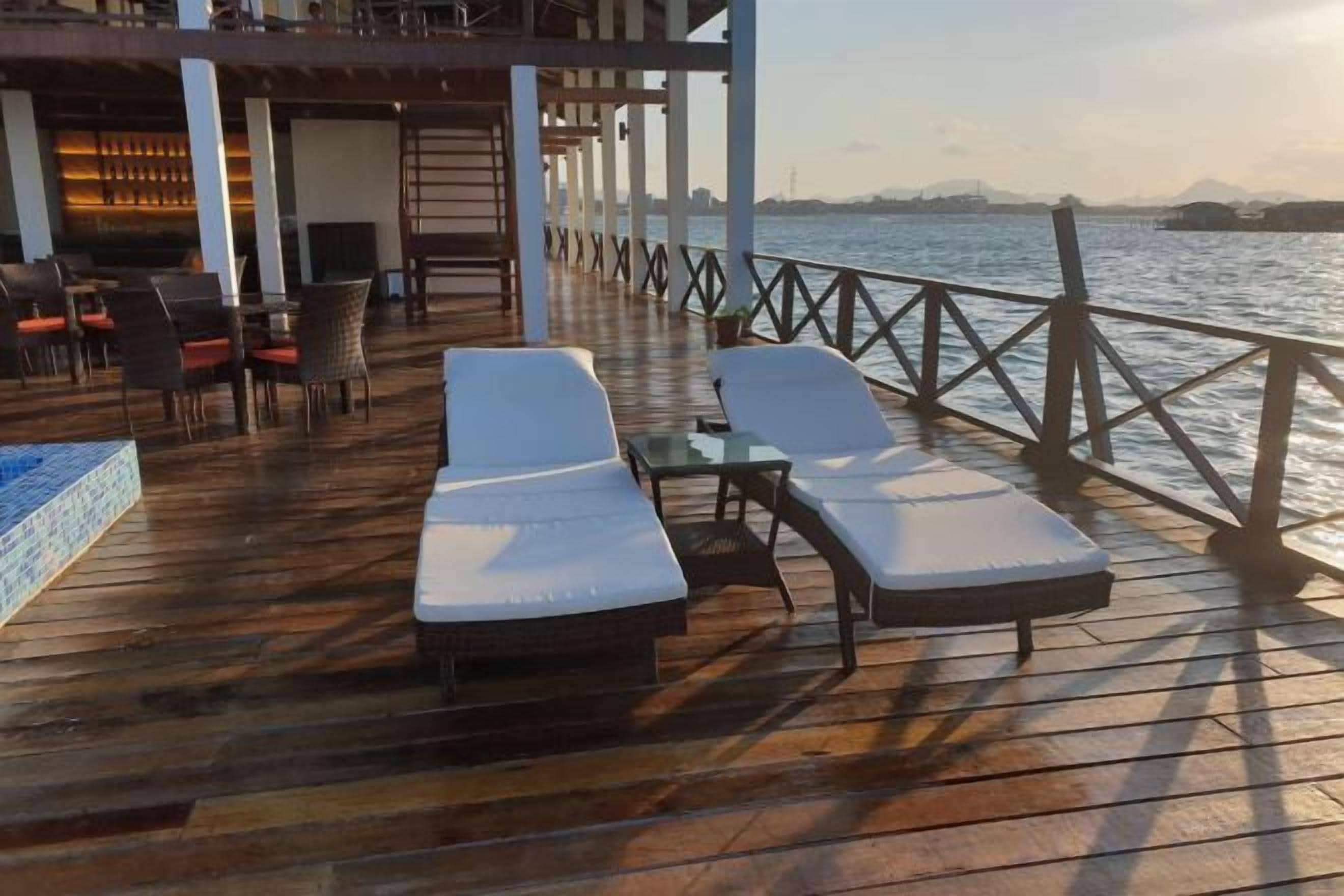 A wooden deck with lounge chairs and a pool table, overlooking a body of water.