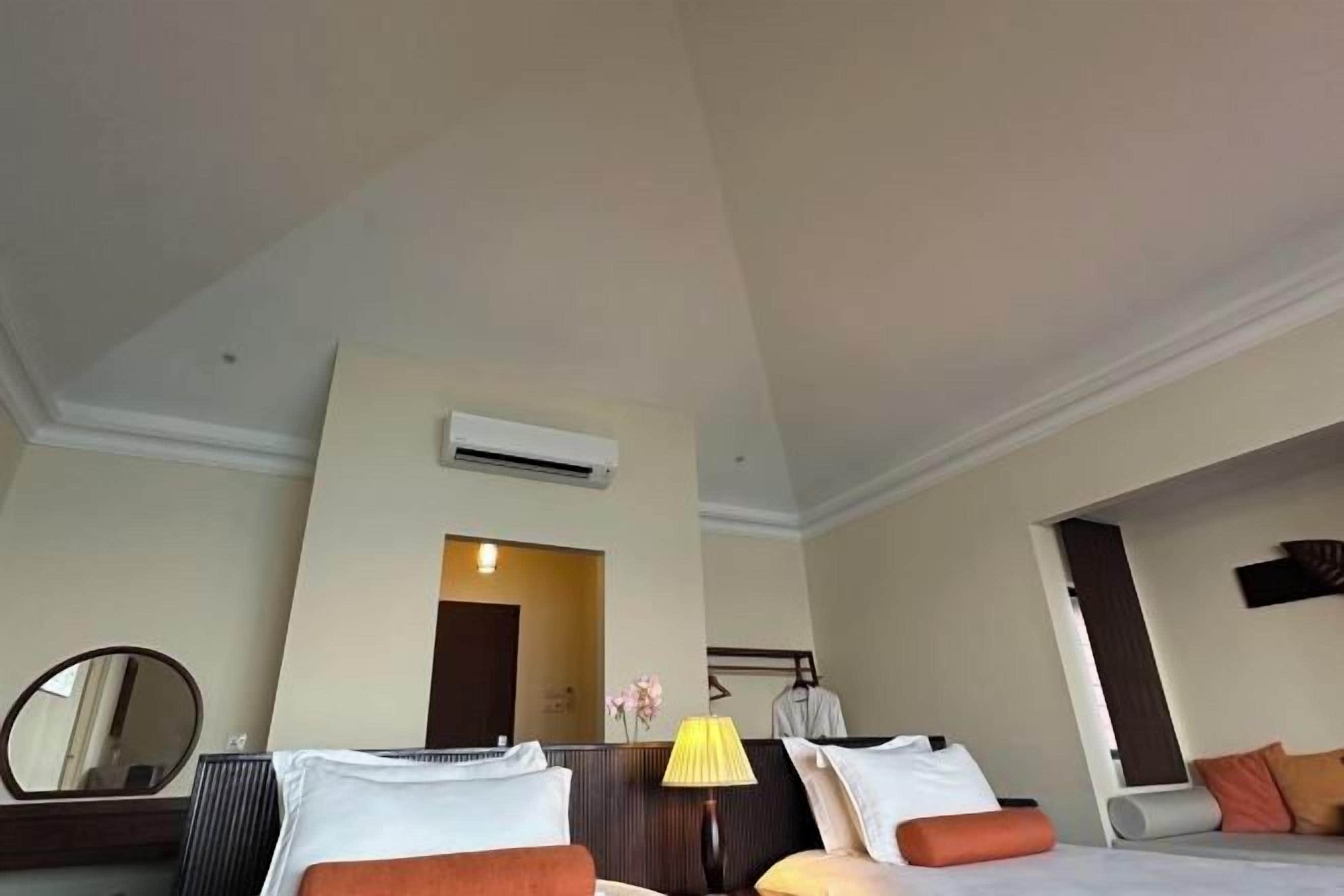 A hotel room with a bed, a bedside table with a lamp, a mirror, and a door leading to another room.