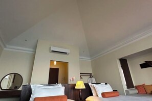 Une chambre d’hôtel avec un lit, une table de chevet avec une lampe, un miroir et une porte donnant sur une autre pièce.