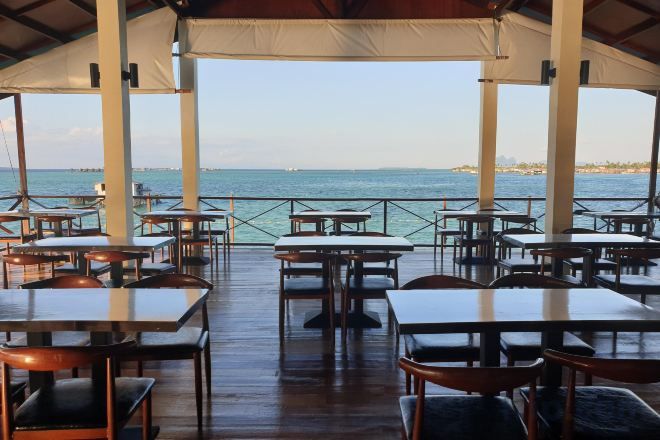 Ein Essbereich im Freien mit Tischen und Stühlen, einer Holzterrasse und Blick auf das Meer.