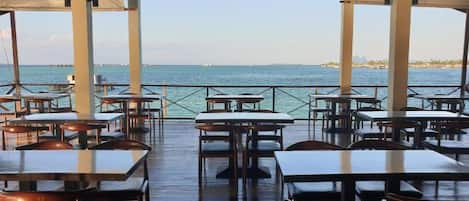 Un área de comedor al aire libre con mesas y sillas, una terraza de madera y vistas al mar.