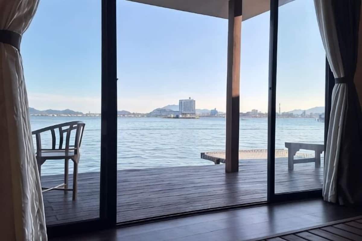 Une pièce avec vue sur un plan d’eau, une terrasse en bois et deux chaises.