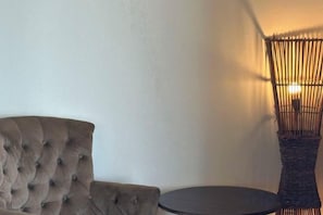 A tufted armchair and a round table in a room with a plain wall and a woven chair. - Sea Star Resort Semporna (Semporna)