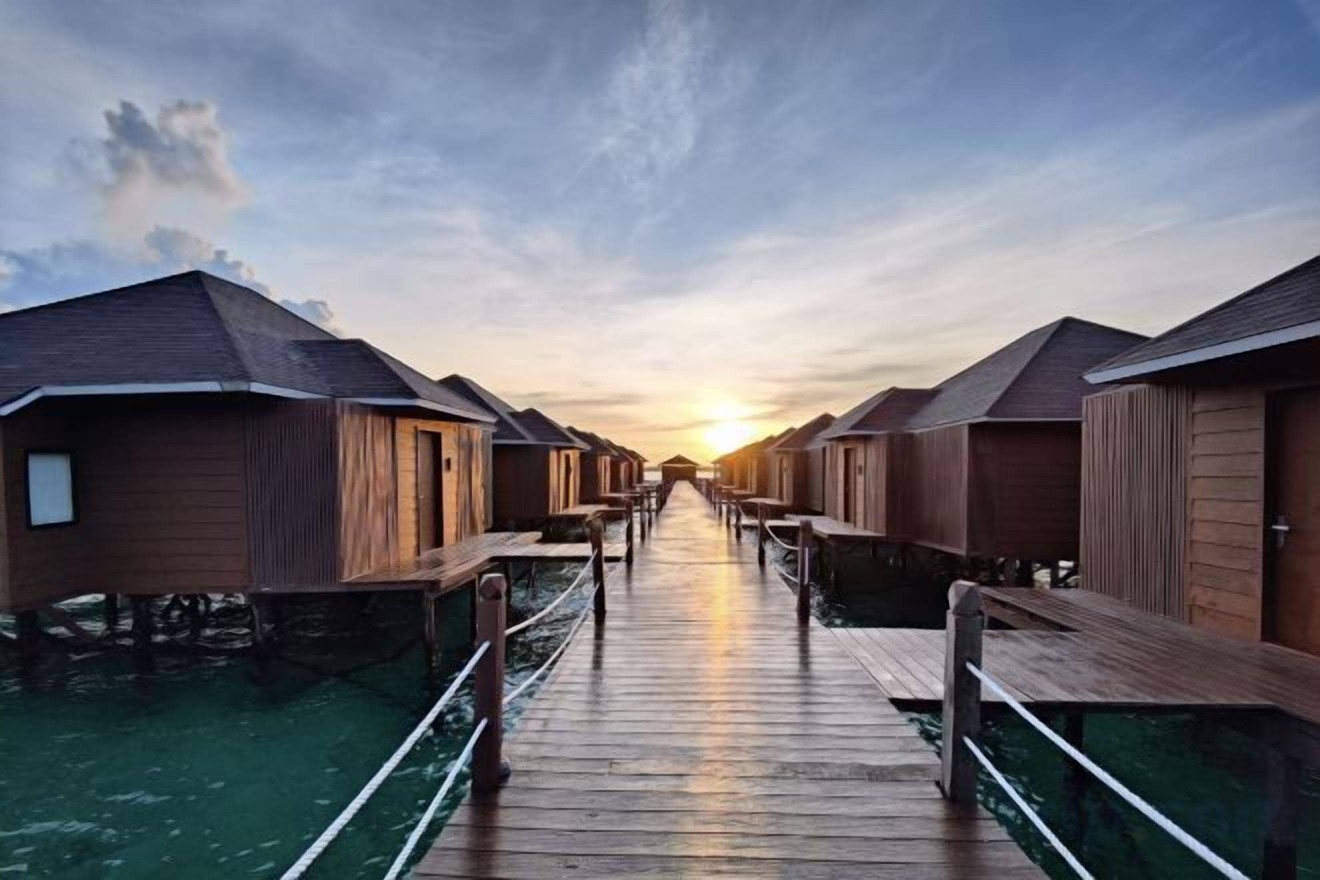 A wooden walkway leading to overwater bungalows with a sunset in the background.