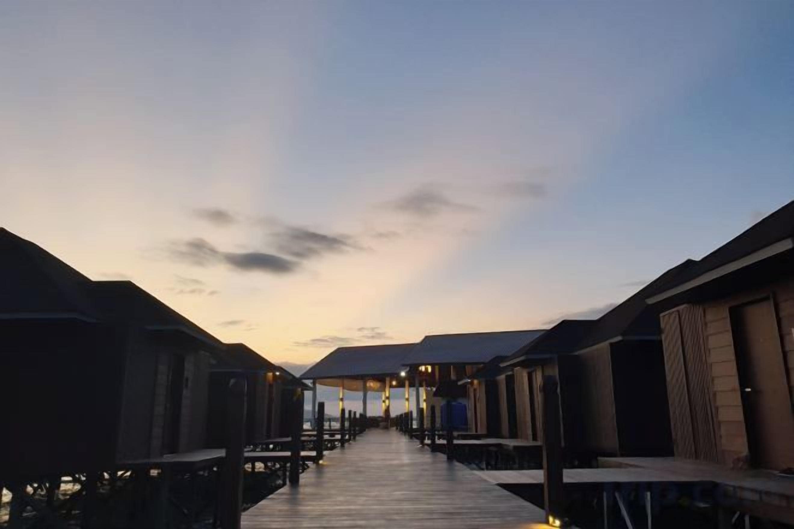 Ein Holzsteg führt zu überwasserbungalows, der Himmel darüber ist klar.