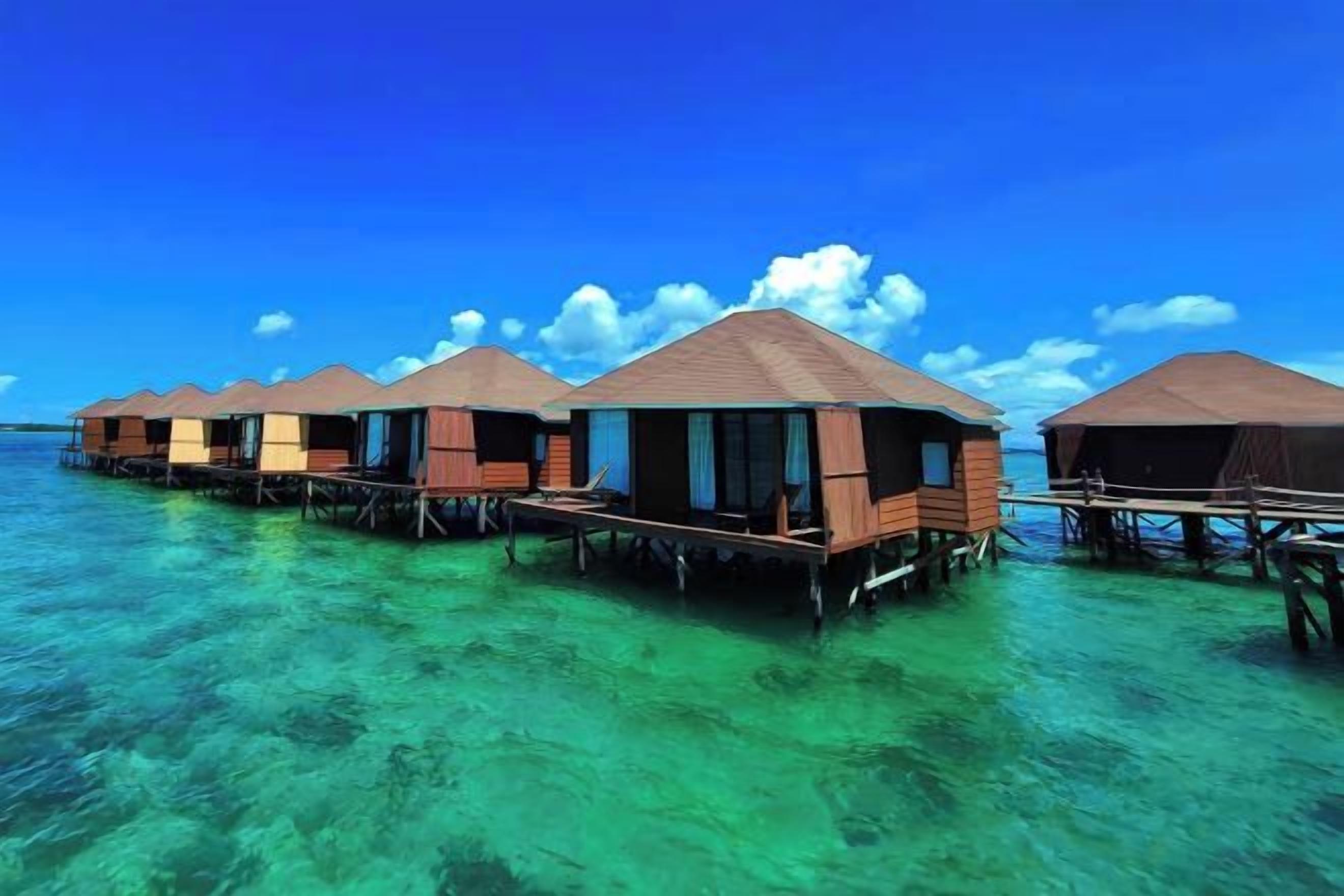 Bungalow sull'acqua con strutture in legno e pareti aperte, galleggianti su acque cristalline turchesi.