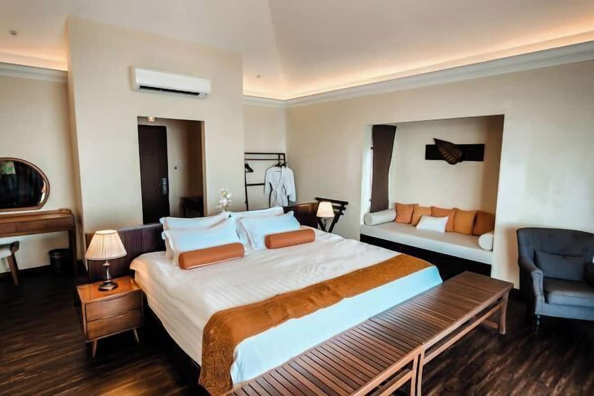 Une chambre d’hôtel avec un grand lit, des tables de chevet, un banc, une chaise, un bureau et une armoire.