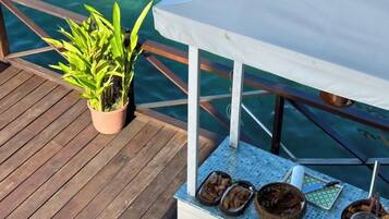 Une terrasse en bois agrémentée d’une plante en pot, une table recouverte d’une nappe blanche et un saladier en métal.