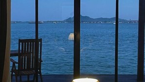 Μια θέα από ένα δωμάτιο με ένα μεγάλο παράθυρο που βλέπει σε μια έκταση νερού, μια καρέκλα και ένα φωτιστικό.