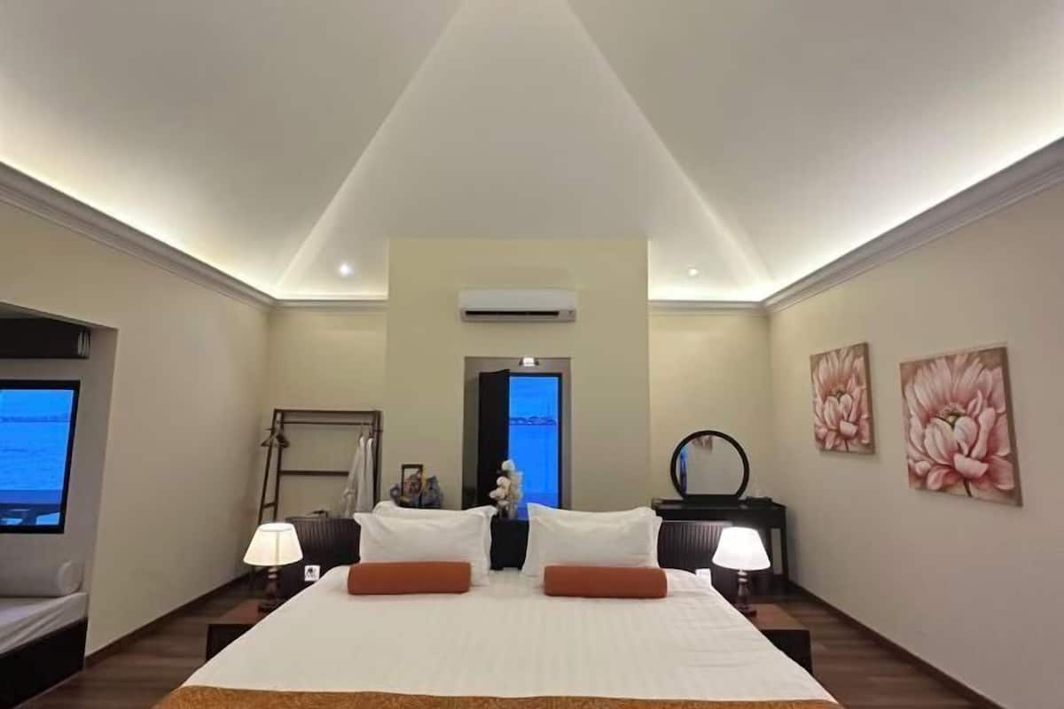 Une chambre d’hôtel avec un grand lit, deux tables de chevet avec des lampes, un téléviseur à écran plat, un appareil de climatisation et une porte donnant sur une autre pièce.