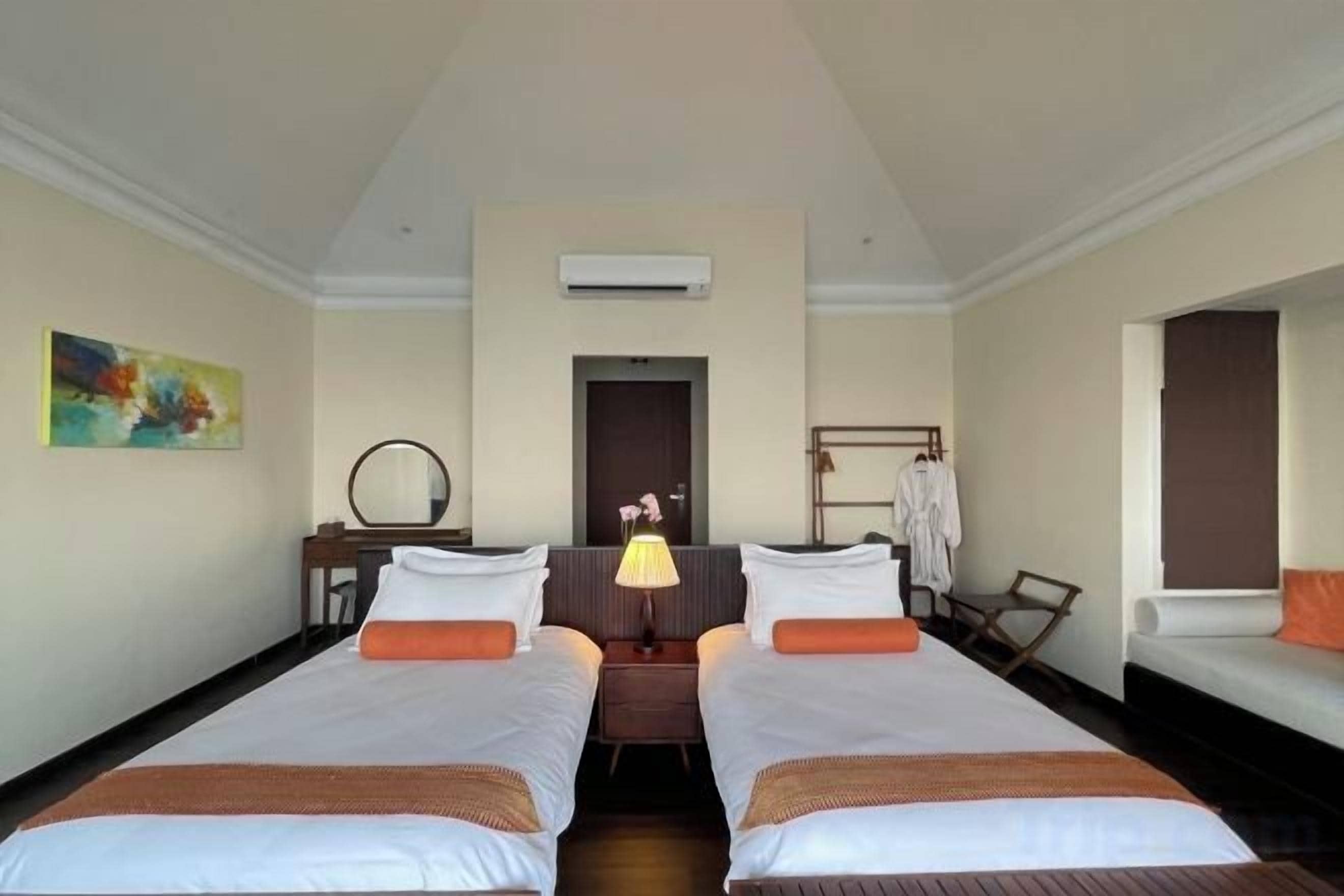 A hotel room with two beds, a desk, a chair, and a mirror.