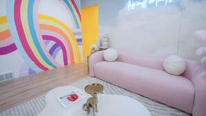 Un soggiorno moderno con un murale colorato a forma di arcobaleno, un neon, un divano rosa e un tavolino con oggetti decorativi.