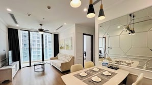 A modern living room with a dining area, large windows, a ceiling fan, and a large mirror.