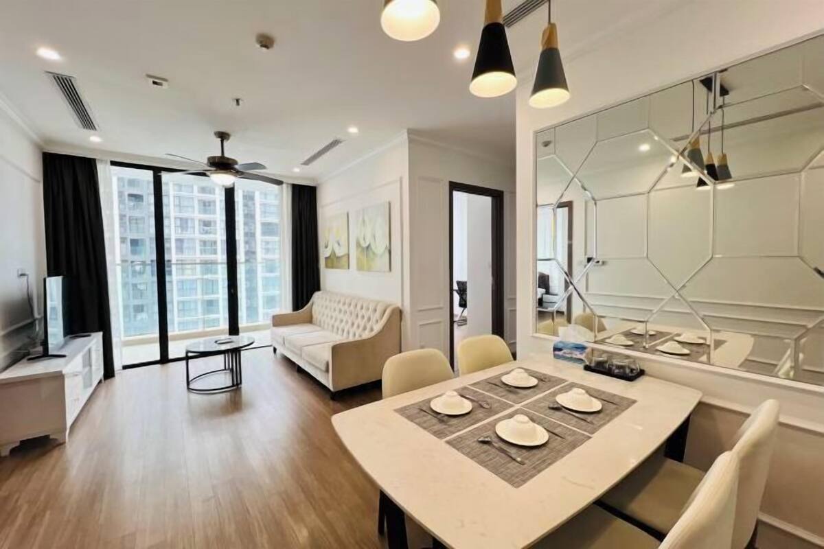 Un salon moderne comprenant un coin repas, de grandes fenêtres, un ventilateur de plafond et un grand miroir.