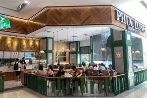 Un café avec un comptoir et un espace pour s’asseoir, des clients à l’intérieur et une enseigne au-dessus du comptoir.