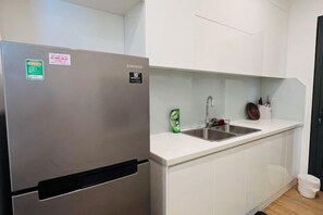 A kitchen with a stainless steel refrigerator, a white countertop, a sink, and a cabinet.