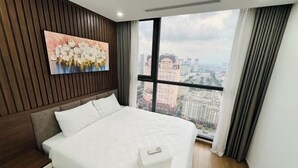 A modern hotel room with a large bed, a city view through a large window, and a wall-mounted painting.