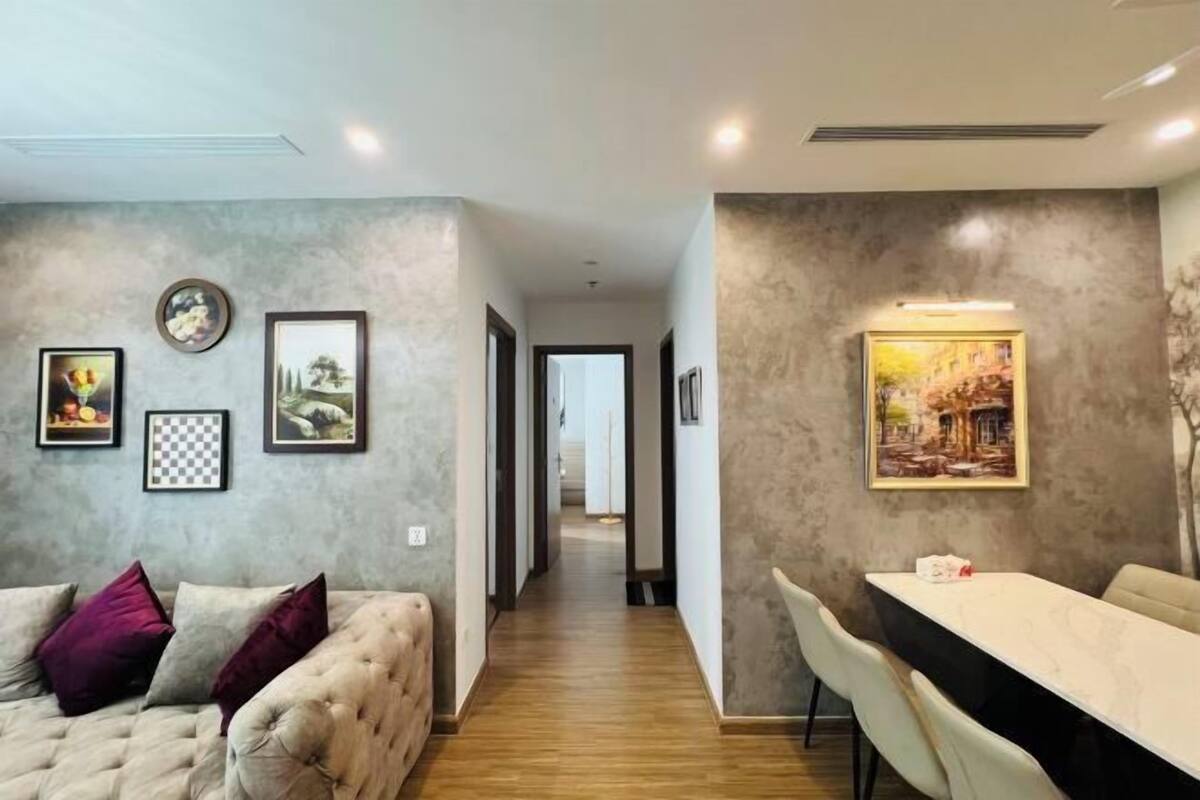 Un salon moderne avec un canapé, une table à manger et des chaises. Les murs sont ornés de tableaux encadrés, et un couloir mène à une autre pièce.