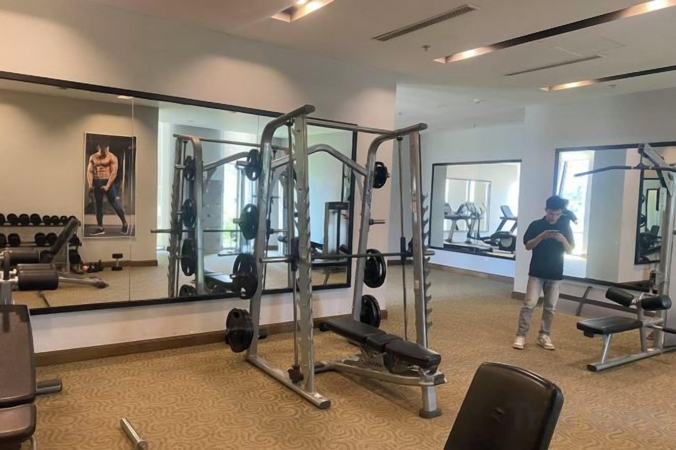 A gym with weightlifting equipment, a bench, and a mirror reflecting the space.