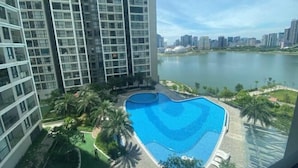 A high-rise building with a swimming pool surrounded by greenery and a view of a lake.