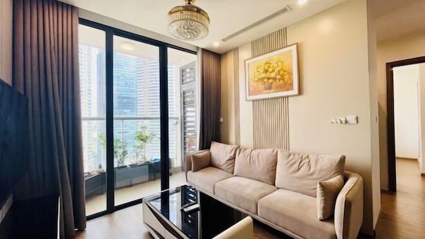 A modern living room with a sofa, a glass coffee table, and a large window offering a city view.