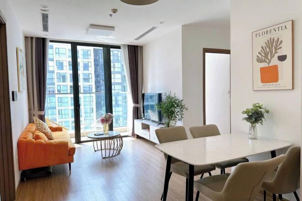Un salon moderne avec un canapé, une table à manger et des chaises. Une grande fenêtre offre une vue sur les immeubles.