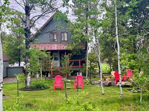 A cabin with a porch, surrounded by trees and a grassy yard.