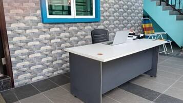 A reception desk with a computer, a chair, and a small table with items on it.