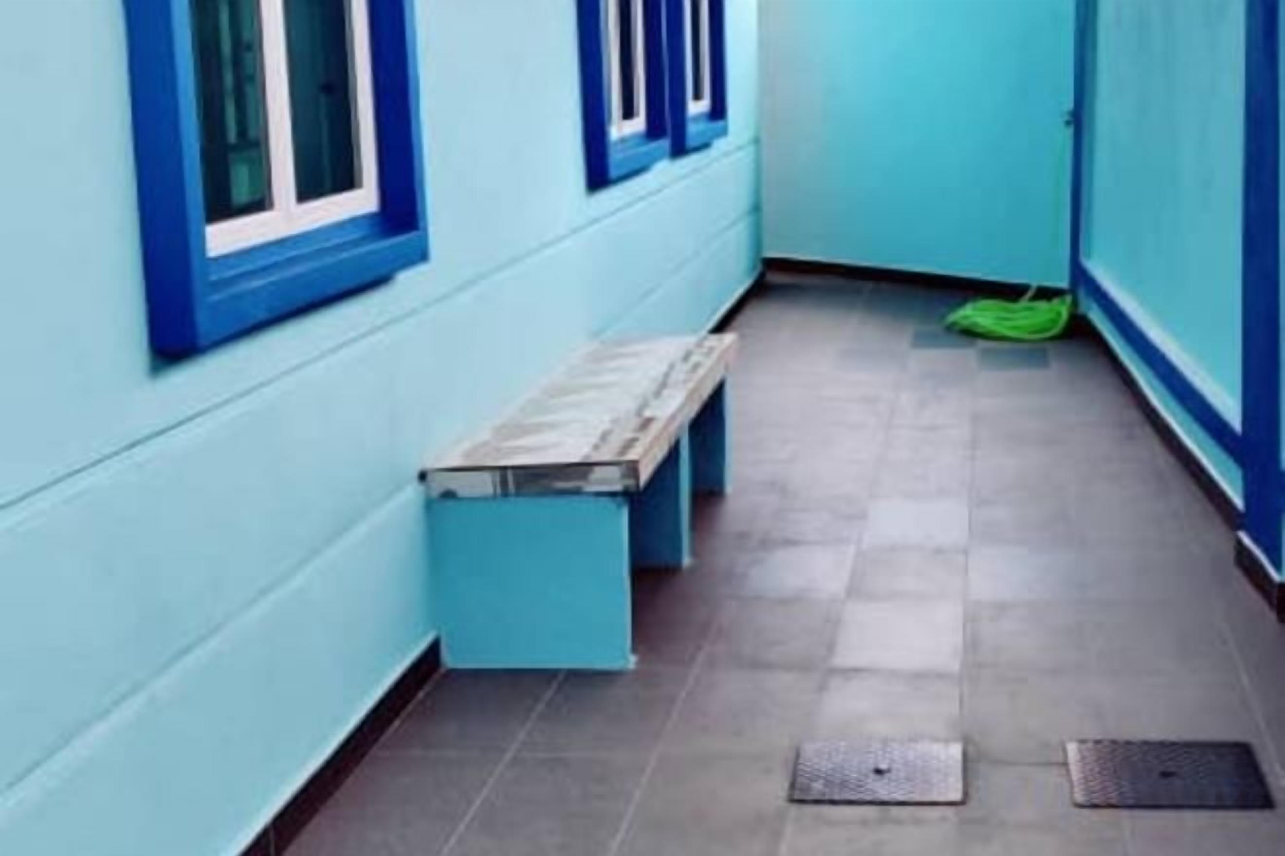 Un couloir étroit aux murs bleus, avec un banc.