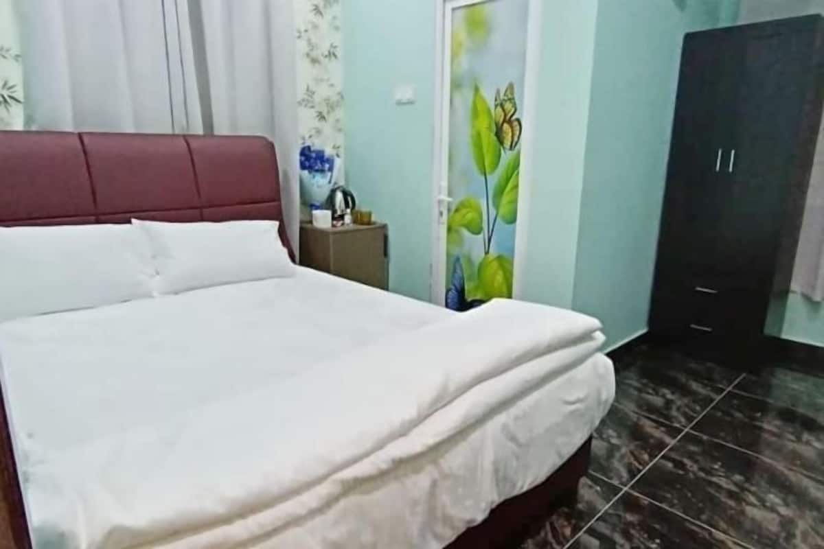 A bed with white linens, a red headboard, a small bedside table with a lamp, and a wardrobe with two doors.