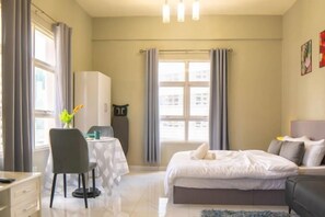 A bedroom with a bed, a desk, and a chair. There is a window with curtains, a radiator, and a wall-mounted TV. - MayTower by Horizon Homes (Kuala Lumpur)