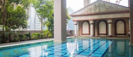 Una piscina interior con suelo de baldosas, rodeada de columnas y un edificio con tejado de cerámica.