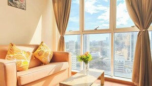 A living room with a sofa, a coffee table, and a view of a cityscape through large windows. - MayTower by Horizon Homes (Kuala Lumpur)