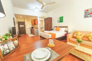 A hotel room with a bed, a sofa, a dining table with a plate and a cup, a TV, and a ceiling fan. - MayTower by Horizon Homes (Kuala Lumpur)