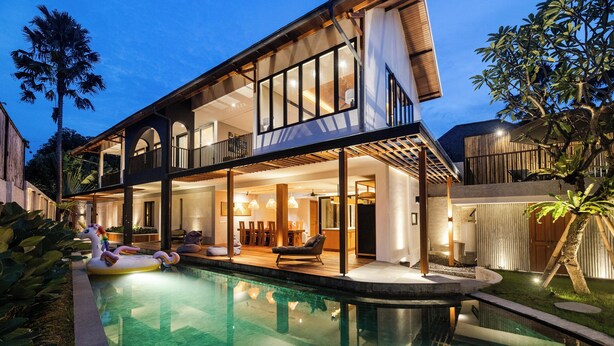 Una casa moderna de dos pisos con piscina, mobiliario exterior y un balcón grande.