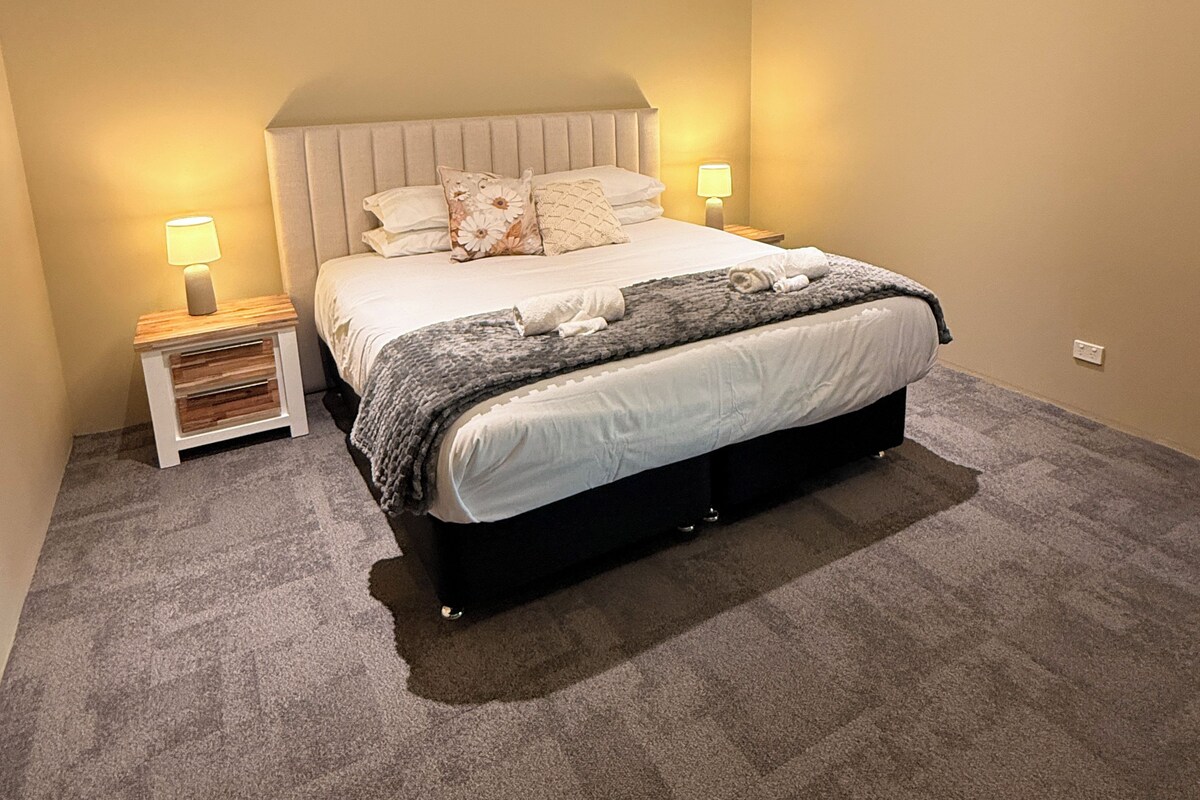 A bedroom with a bed, bedside lamps, a ceiling fan, and a carpeted floor.