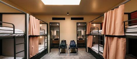 A dormitory room with bunk beds, a skylight, a mirror, and a small table with a backpack.