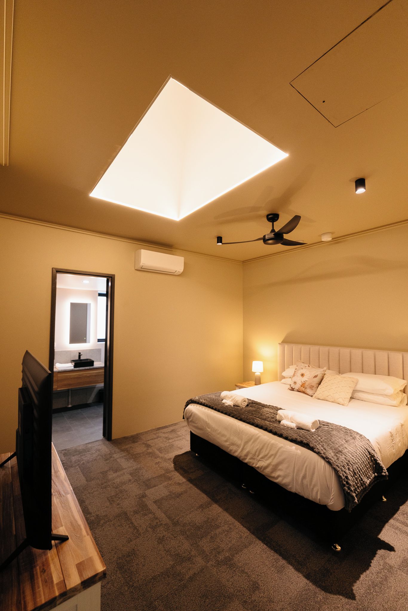 A hotel room with a bed, a ceiling fan, a flat-screen TV, and a skylight.