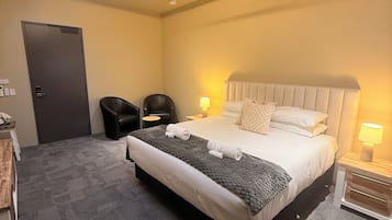 A hotel room with a bed, a ceiling fan, a door, and a small table with a lamp.