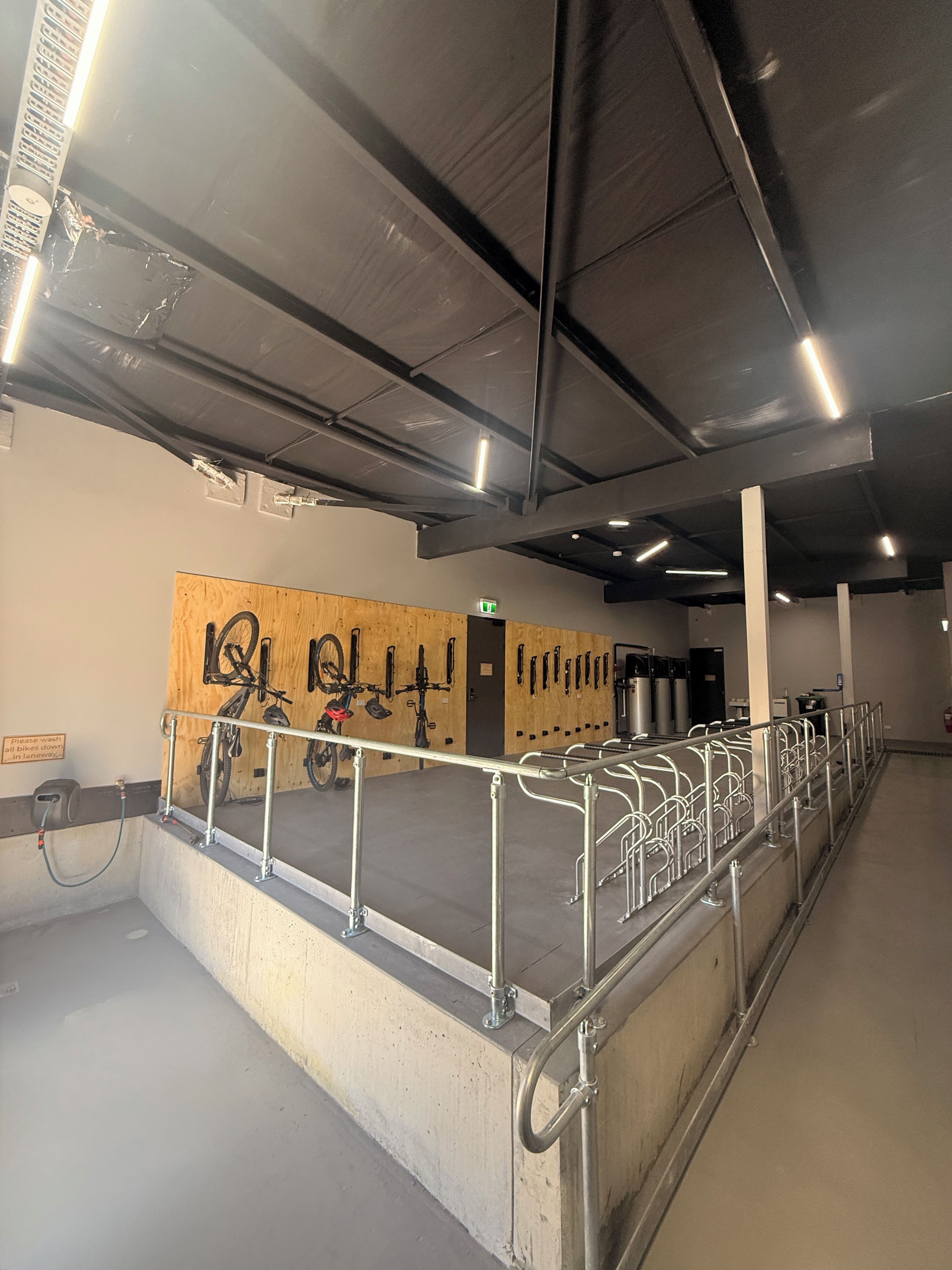 A clean, well-lit indoor space with metal railings, a wooden wall with bike racks, and a concrete floor.