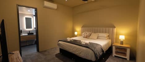 A bedroom with a bed, bedside tables, a ceiling fan, and a bathroom visible through an open door.