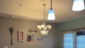 Comedor con mesa y sillas de madera, una araña y una pared decorada.