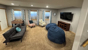 Una sala de estar con un sofá, dos sillones estampados, un sillón de peluche, una mesa de centro, un televisor y un reloj en la pared.