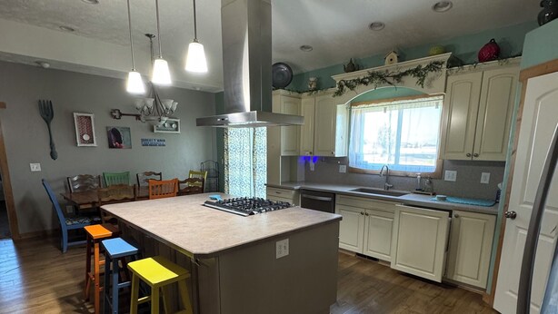 Una cocina con isla central, suelo de madera, armarios blancos e iluminación colgante.