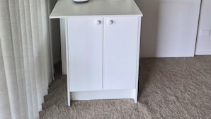 Een compacte kitchenette met een wit aanrecht, een broodrooster, een waterkoker en een klein kastje.